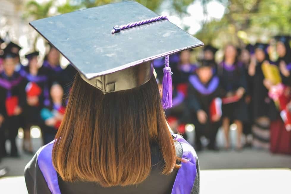A girl in cap and gown at graduation facing a crown